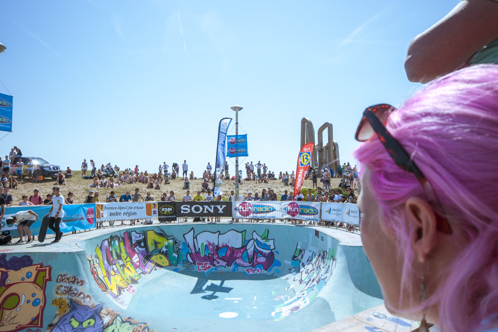 Une jeune femme à la chevelure rose fluo, le regard tourné vers le bowl du Skate Park du Prado lors de la Sosh FreeStyle Cup.